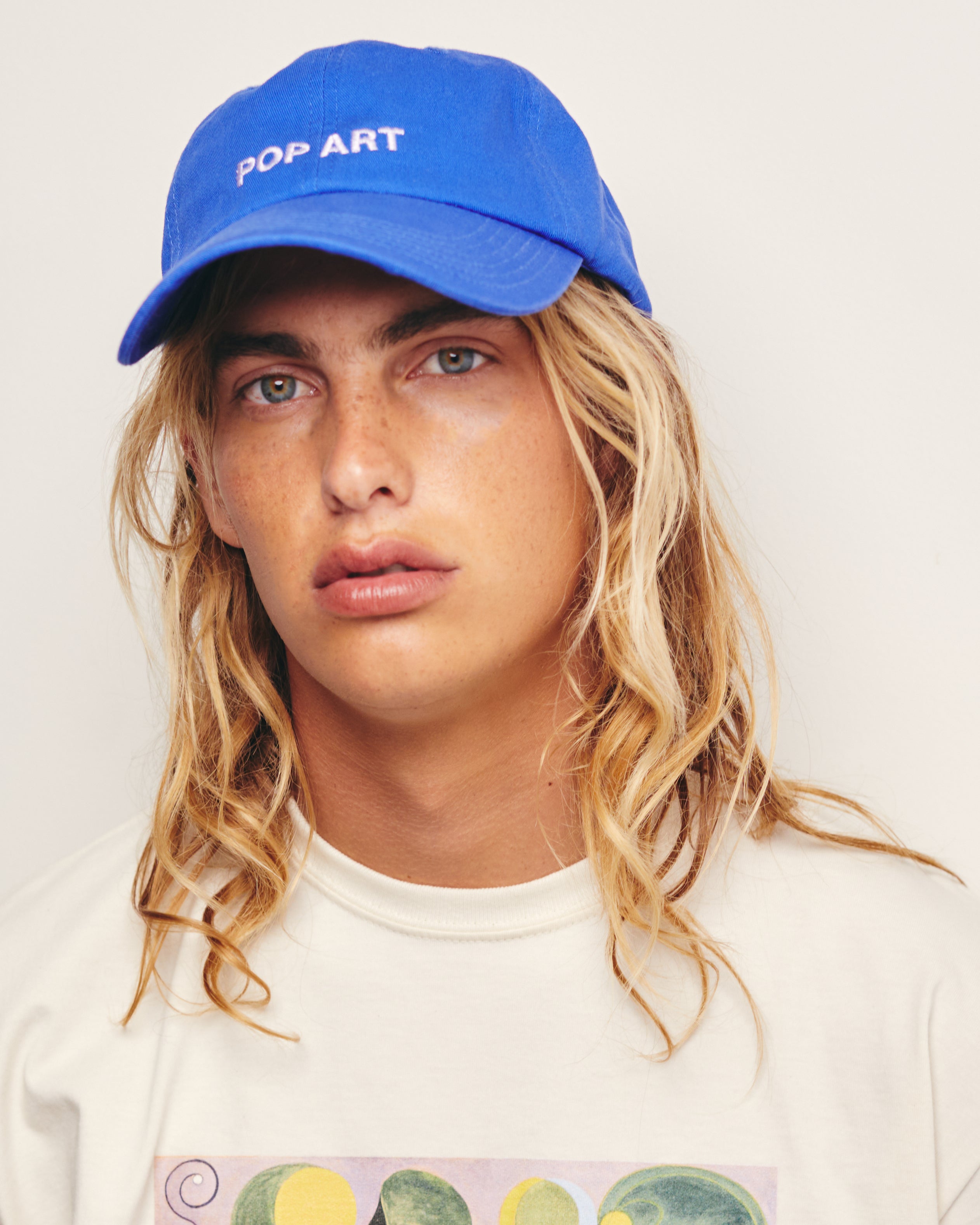 Lucas Ucedo wears Blue Baseball Cap / Dad Hat with Pop Art Movement Text Embroidery on Front. 100% Cotton.